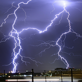 A lightning strike fills the sky with a cityscape silhouetted in the foreground.