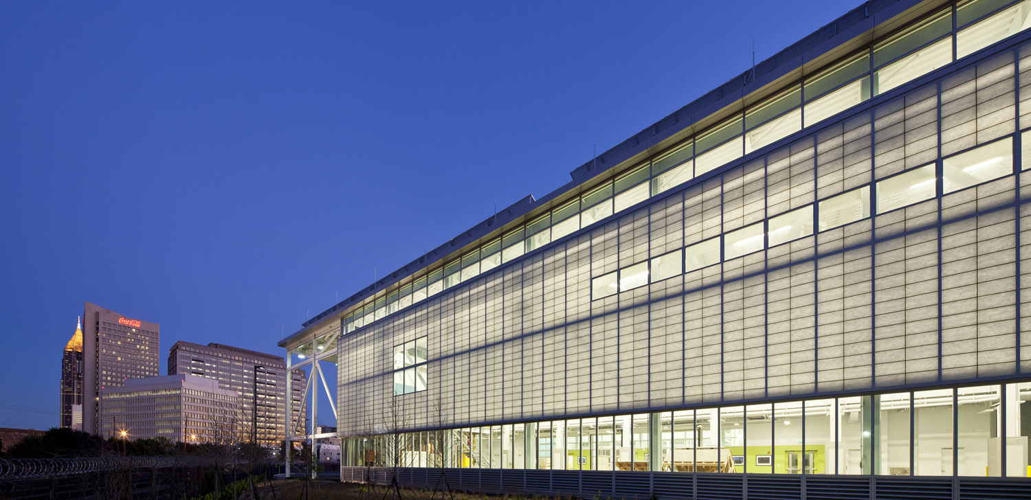 Image of the Carbon Neutral Energy Solutions building at Georgia Tech, at night, lit from within, with the ATL skyline in the background.