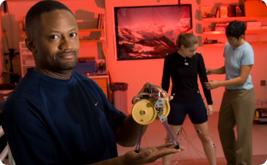 researcher shows a device while students work in background