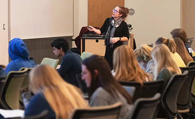 Image link-Education. Picture of a woman delivering a lecture to students in a university classroom.