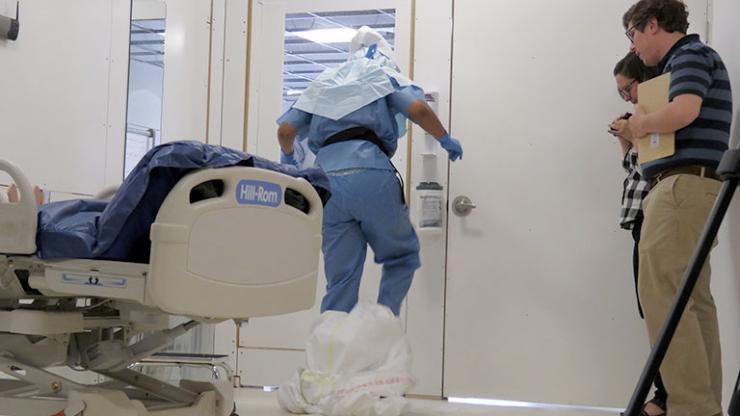 <p>A researcher observes a doffing simulation in a mock-up of a biocontainment unit.</p>