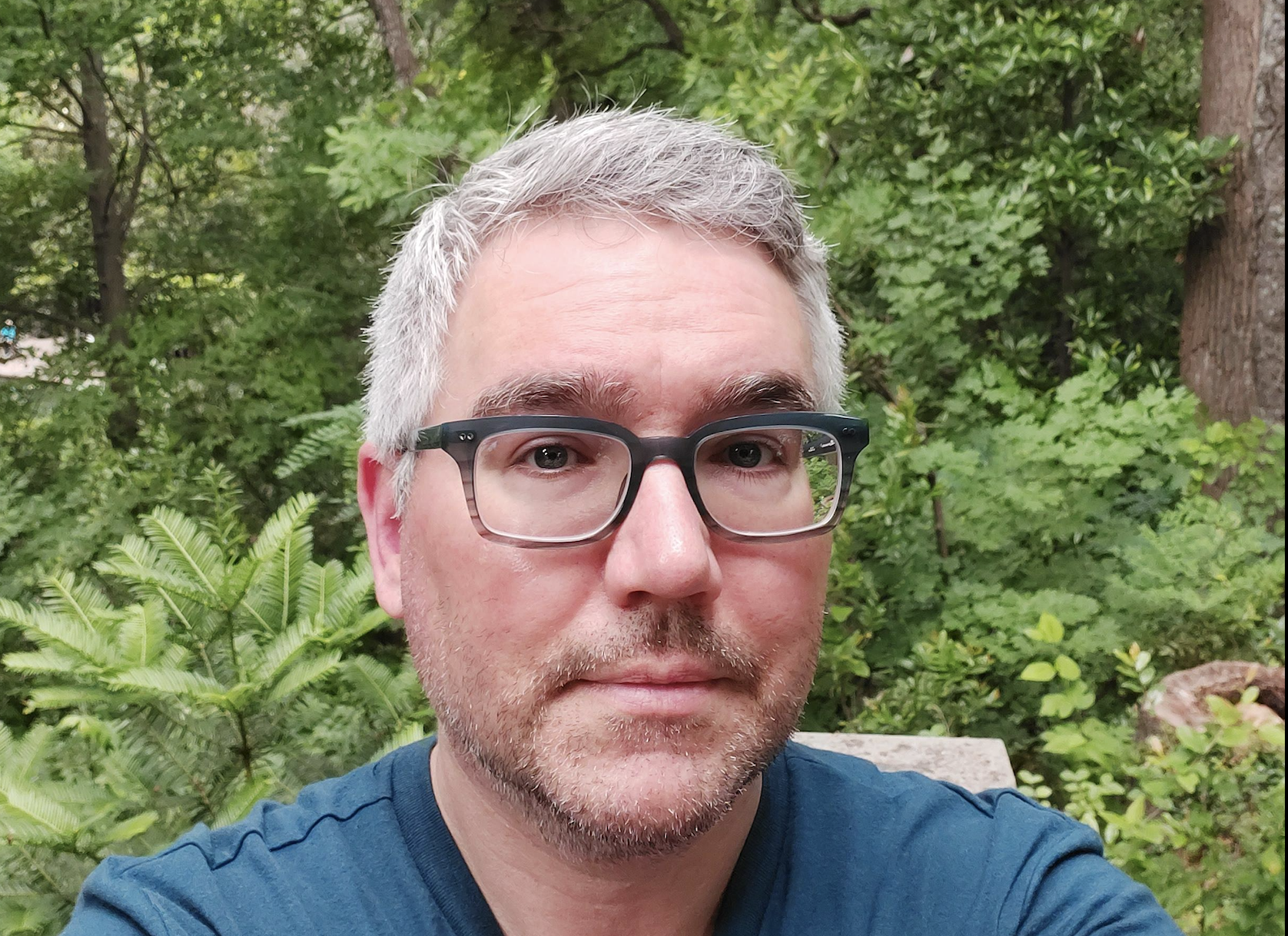 A man with glasses in front of greenery