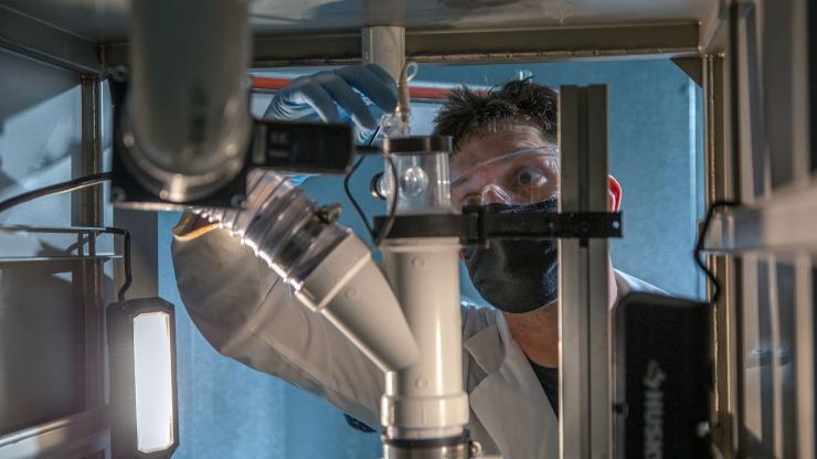 <p>Seth Stewart, a graduate research assistant in Georgia Tech’s School of Mechanical Engineering, adjusts equipment designed to sample building air for the presence of the SARS-CoV-2 virus that causes COVID-19. Particles from the air would be concentrated and then analyzed using a sensor that captures and detects the presence of virus particles. (Credit: Christopher Moore, GTRI)</p>