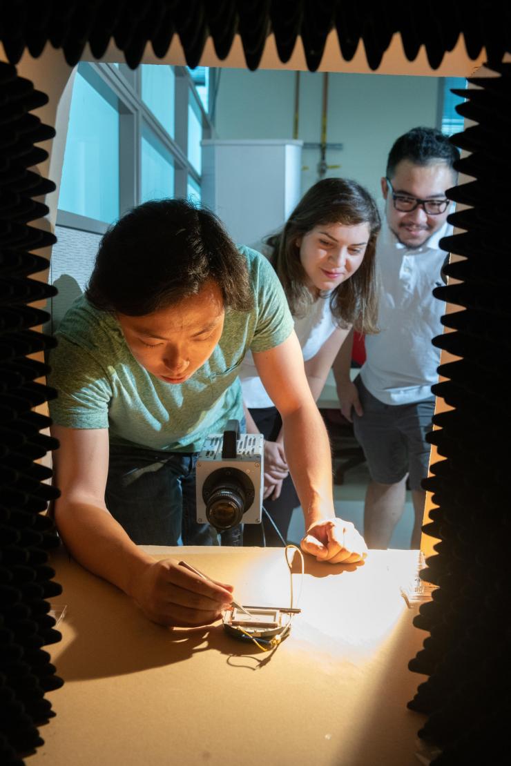 <p>Georgia Tech researchers Azadeh Ansari, DeaGyu Kim and Zhijian (Chris) Hao test a micro-bristle-bot in a chamber designed to contain the sound of the piezoelectric actuator. (Photo: Allison Carter, Georgia Tech)</p>