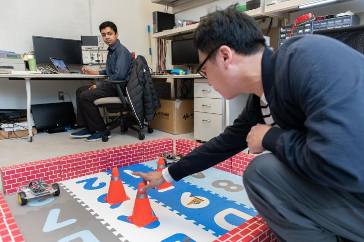 <p>Georgia Tech Researcher Ningyuan Cao places a robotic car controlled by an ultra-low power hybrid chip into a test arena where it will demonstrate its ability to learn and collaborate with another robot. (Photo: Allison Carter, Georgia Tech)</p>