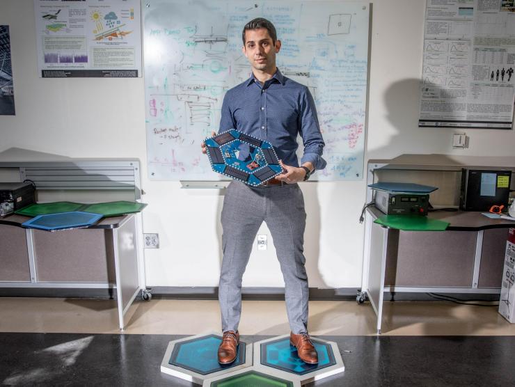 <p>Ilan Stern, a GTRI senior research scientist, stands on piezoelectric tiles that will be used to create a lighted outdoor footpath at the NASA Kennedy Space Center’s Visitor Complex at Cape Canaveral, Florida. He’s holding the electronic components used in the tiles. (Credit: Branden Camp, Georgia Tech)</p>