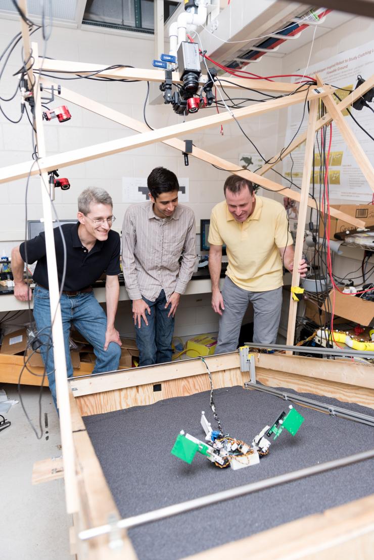 <p>Researchers (l-r) Richard Blob, Ben McInroe and Dan Goldman examine a robot named MuddyBot whose locomotion was inspired by the mudskipper. The robot has two limbs and a powerful tail to move though a trackway that can be raised to simulate granular slopes. Blob is a professor at Clemson University; McInroe was a student at Georgia Tech when the research was conducted, and Goldman is a professor at Georgia Tech (Credit: Rob Felt, Georgia Tech)</p>