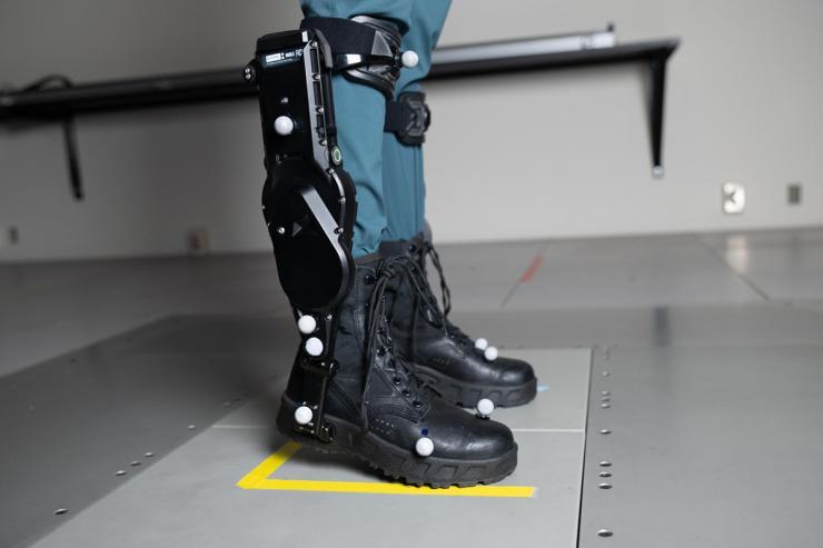 A person wearing black robotic exoskeleton boots standing on a gray platform.