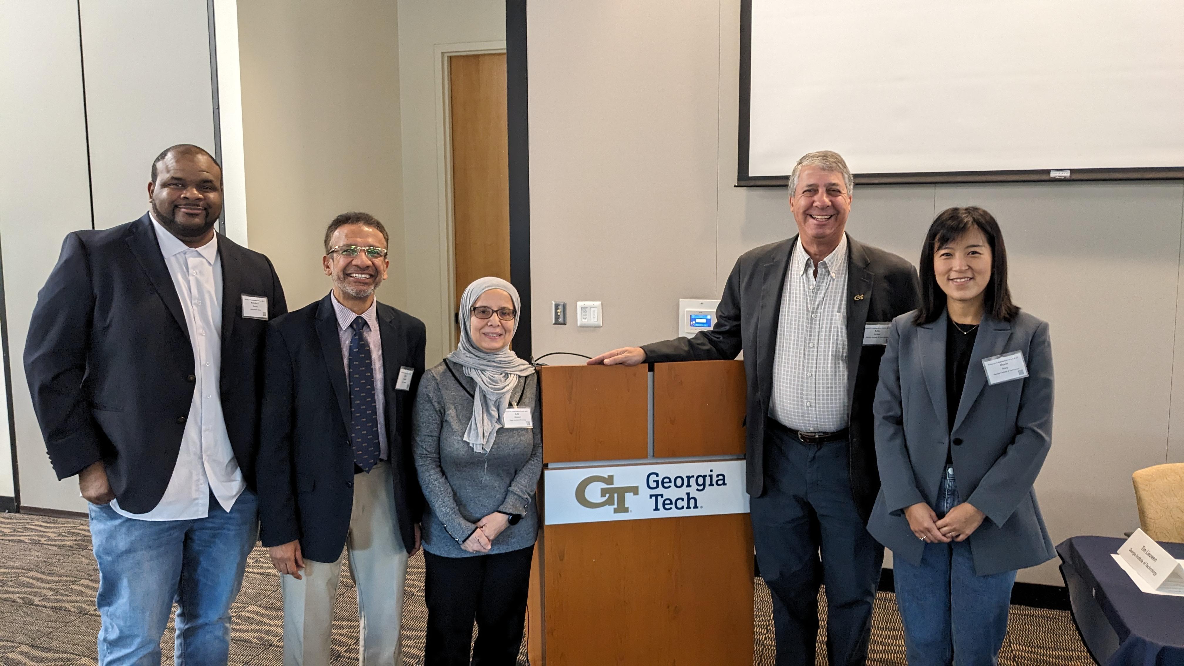 Five people stand in a room next to a podium. 