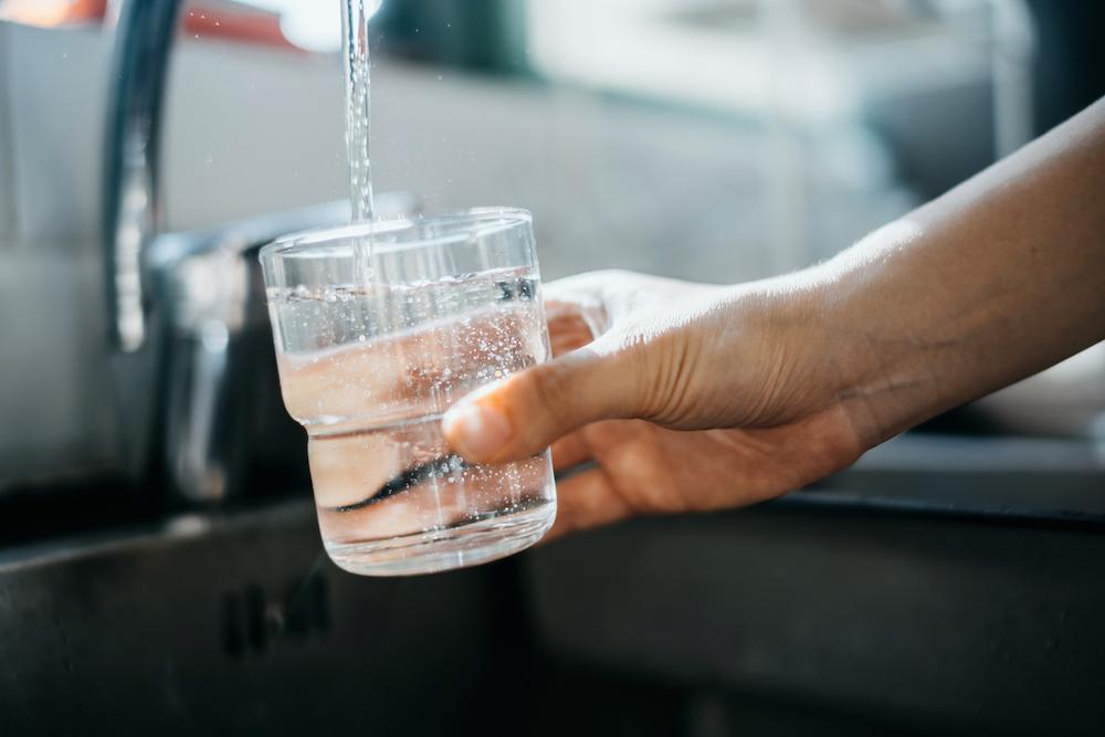 Hand holds glass over faucet