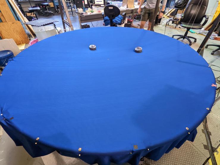 <p>Two small robots move on a stretchy, trampoline-like surface.</p>