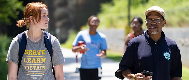 Photo Credit Ben Gray, AJC. A student wearing a "Serve-Learn-Sustain" tee shirt walks along a campus walkway with a Georgia Tech faculty member.