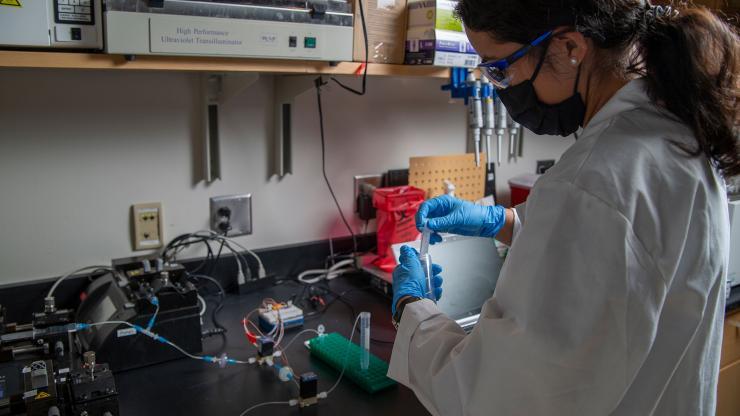 <p>Nina Sara Fraticelli-Guzman, a graduate research assistant in Georgia Tech’s School of Mechanical Engineering, demonstrates a microfluidic system that would concentrate fluid samples containing particles collected from building air. In a fully operating system, the fluid would be analyzed for the presence of SARS-CoV-2, the virus that causes COVID-19. (Credit: Christopher Moore, GTRI)</p>