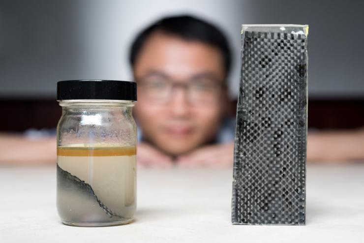 <p>Kai Yu, a former postdoctoral researcher in The George W. Woodruff School of Mechanical Engineering at Georgia Tec, sits behind a piece of carbon fiber composite immersed in alcohol. (Credit: Rob Felt, Georgia Tech)</p>