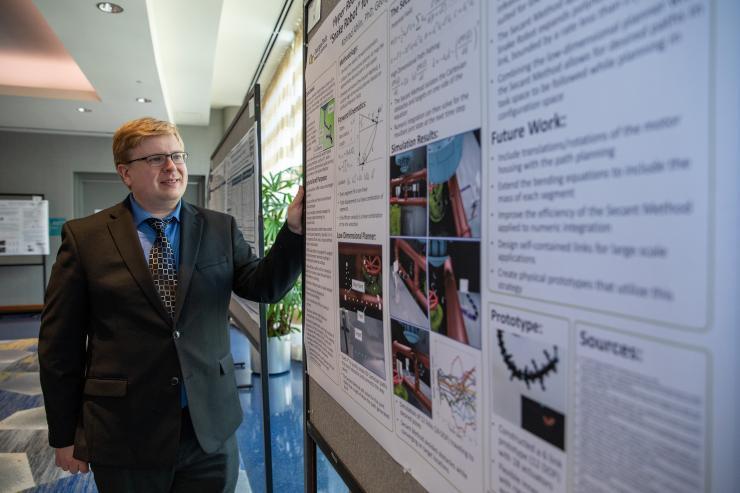 <p>GTRI Research Engineer Konrad Ahlin explains a poster on his "Hyper Redundant Flexible Manipulator (HRFM)" at the recent DARPA Forward conference held at Georgia Tech. (Credit: Sean McNeil, GTRI)</p>