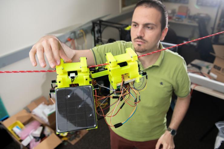 <p>Graduate Research Assistant Gennaro Notomista shows the components of SlothBot on a cable in a Georgia Tech lab. The robot is designed to be slow and energy efficient for applications such as environmental monitoring. (Photo: Allison Carter, Georgia Tech)</p>