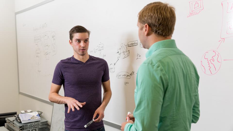 Two people discussing in front of a white board
